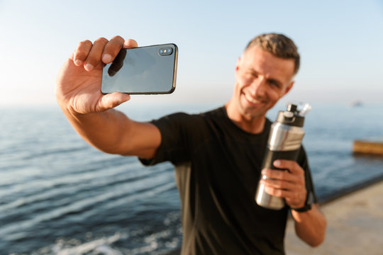 Mature sportsman take a selfie with bottle of water on the beach.
