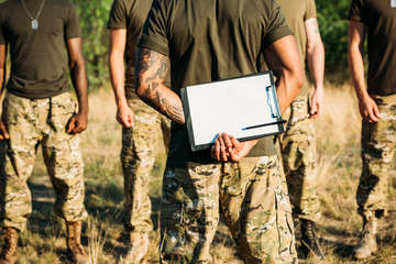 partial view of tactical instructor with notepad and multiracial soldiers in military uniform on...