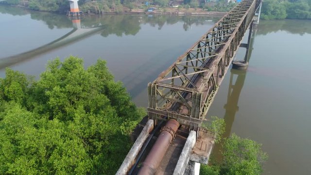 Aerial view. Rusty metal truss aqueduct over the water. Water supply through the pipe from one Bank of the river to another. Flying around aqueduct quickly. Shooting with a drone.