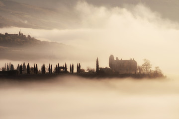 Beautiful foggy sunrise in Tuscany, Italy with cypresses and house. Natural misty background
