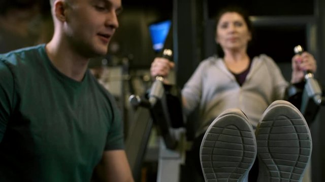 Tracking shot of concentrated woman trying to do leg raises with dip station during workout at the gym, male coach helping her