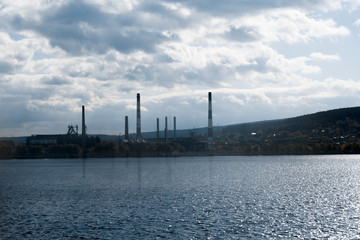 Fototapeta na wymiar tubes of factory on a background of water and sky, environmental pollution concept