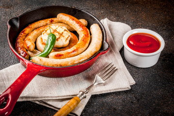 Homemade grilled beef and chicken sausages in red cast iron frying pan, with ketchup,
