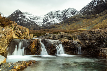 Fototapeta na wymiar Fairy Pools waterfall, River Brittle,. Glenbrittle, Isle of Skye, with snow covered mountains in the background