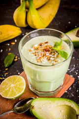 Healthy summer drink, avocado and banana smoothie with lime, granola and coconut milk, dark rusty background copy space