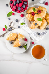 Sweet summer dessert, homemade baked mini croissants with berry jam, served with tea, fresh raspberries, blueberries and mint. On a white marble table, copy space top view