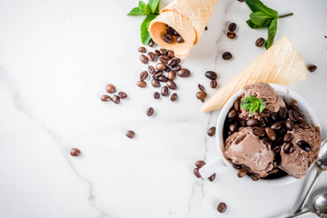 Homemade coffee ice cream, served with coffee beans and mint leaves, with ice cream cones and spoons in the picture. White marble background,