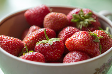 ripe strawberry berry with green leafs in a plate on a green background