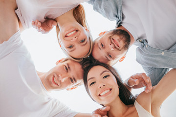 Nice picture of positive teens holding their heads close to each other and looking down on camera. They are smiling. There are two boys and two girls. They are holding each other hands on shoulders.