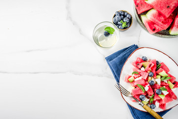 Summer food concept, fresh cold watermelon salad with feta cheese, blueberry, avocado and mint, white marble background copy space