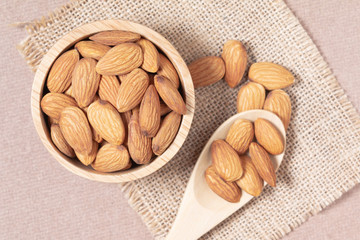 Almond seeds in a cup and spoon are placed on a woven sack and wood table