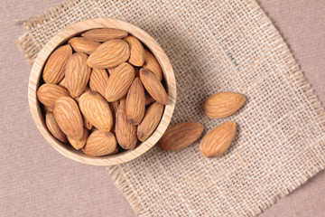 Almond seeds in a cup are placed on a woven sack and wood table