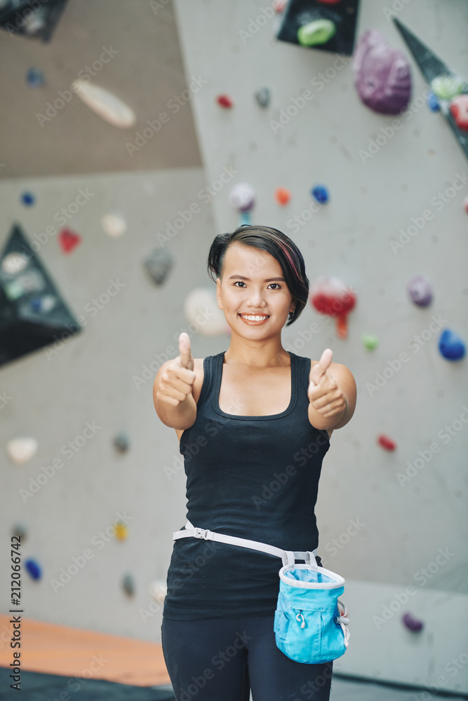 Wall mural Smiling Asian female wearing sportswear standing in climbing club and looking at camera