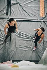 From above shot of young Asian man and woman standing on mat in gym and looking at clambering wall