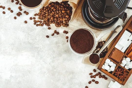 Variety things for prepare coffee. Roasted beans, ground coffee, scoop, electric coffee machine and assortment of sweets and spices to eat with on light background. Top view copyspace
