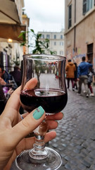 A glass of red wine in a woman's hand in a street cafe, Rome
