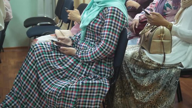 Muslim women in long dresses at the islamic conference uses a smartphones