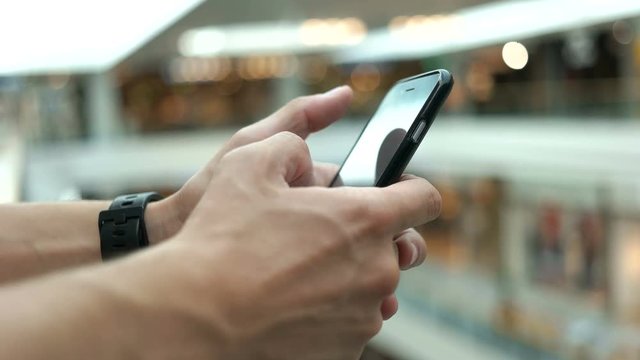 Close up shot of young man using smart phone for chatting with friends on the shopping centre background.