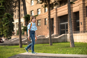Obraz na płótnie Canvas A schoolboy blond, wearing in a shirt and jeans, walks with a knapsack goes by the big ancient building to school.