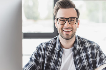 Obraz premium portrait of handsome young man in eyeglasses smiling at camera at workplace