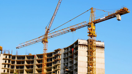 Two tower cranes near building. Construction site. Building under construction.