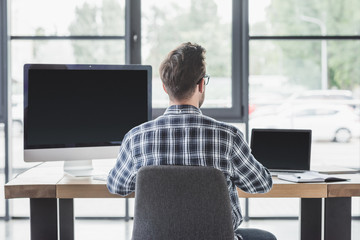 back view of young programmer working with laptop and desktop computer