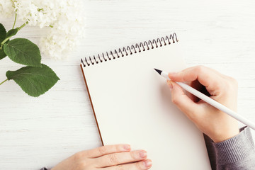 Woman's hand writing in notebook on white wooden table. Working place and planning concept, top...