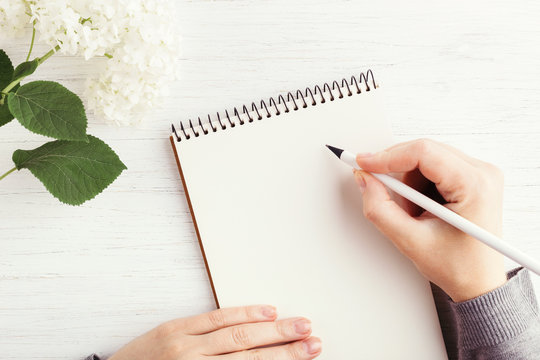 Woman's hand writing in notebook on white wooden table. Working place and planning concept, top view. - Powered by Adobe