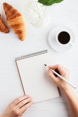 Woman's hand writing in notebook on white wooden table. Working place and planning concept, morning...