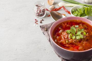 Borsch, beetroot soup in a wooden bowl with fresh herbs on a light background.