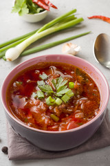 Borsch, beetroot soup in a wooden bowl with fresh herbs on a light background.