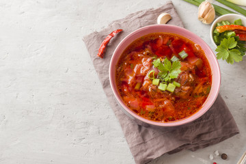 Borsch, beetroot soup in a wooden bowl with fresh herbs on a light background.
