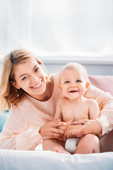 happy mother and child relaxing on bed at home and looking at camera