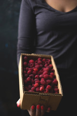A box of fresh raspberries in the hands of a girl