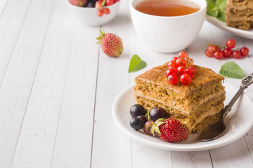 Honey cake with strawberries, mint and currant, a Cup of tea on a light background