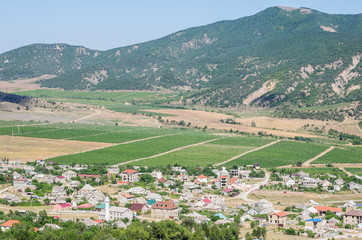 Fototapeta na wymiar Russia, the Republic of Crimea, Sudak city district, Vesyoloe village. 06/08/2018: View of a settlement in a mountain valley: houses, outbuildings, vineyards