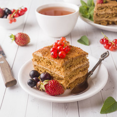 Honey cake with strawberries, mint and currant, a Cup of tea on a light background