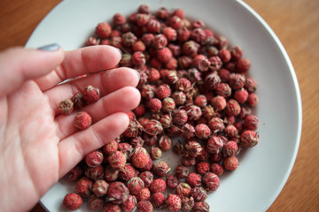 Red field strawberries in hands on white plate on wooden table