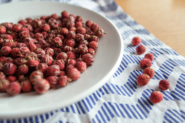 Red field strawberries on white plate on wooden table