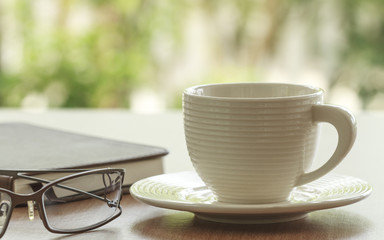 Cup Of Coffee And Eyeglasses With Book On Table In Morning.