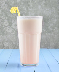 A glass of milkshake with a straw on a pastel color wooden table on the background of a concrete wall.Copy space.