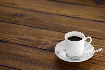 Black coffee with 2 sugars, white cup on a brown wooden table.