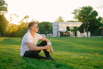 Handsome young hipster man using smartphone outdoors in park with lemonade in his hand