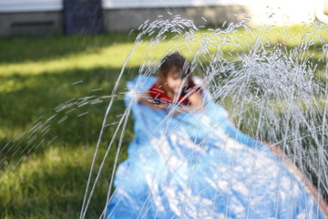 Smiling girl sliding down an outdoor slip and slide. selective focus on water in front of child