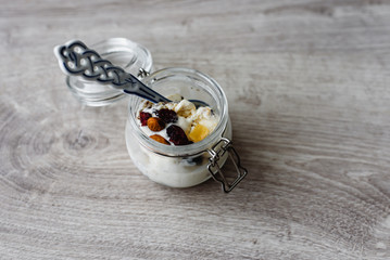 Homemade ice cream in a glass jar, nuts, raisins and a decorative spoon on a wooden background