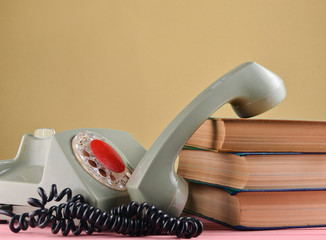 Retro rotary telephone, stack of books on a desk isolated against  pastel wall.