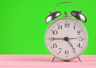 Retro alarm clock stands on wooden table isolated on green, copy space.