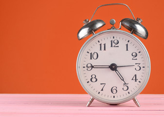 Retro alarm clock stands on wooden table isolated on orange, copy space.