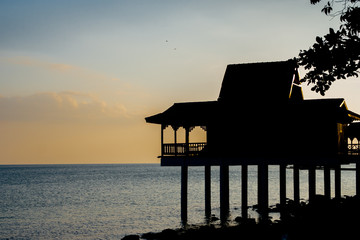 A picturesque scene of the black silhouette of a traditional Malay house on stilts with a...