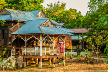 Fototapeta na wymiar A traditional wooden Malay house on stilts with a tropically-suited roof, clothes drying on a clothesline; home of local residents on Langkawi Island, Kedah, Malaysia.